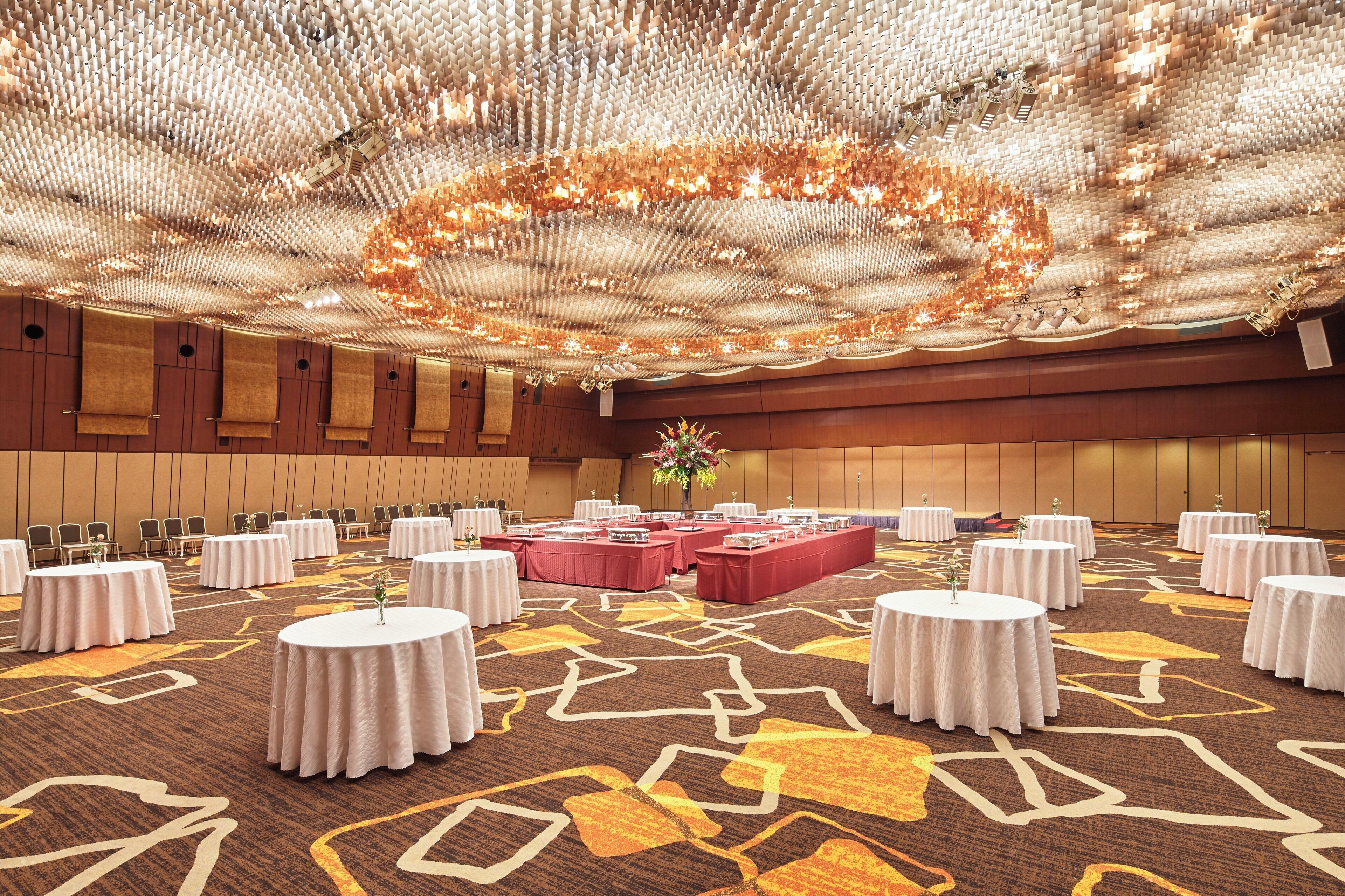 A spacious banquet hall with round tables, a central floral arrangement, and a patterned carpet.