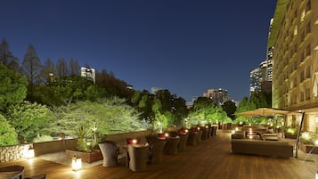 Un bar situé sur un toit, avec une terrasse, entouré de verdure et de bâtiments de la ville.