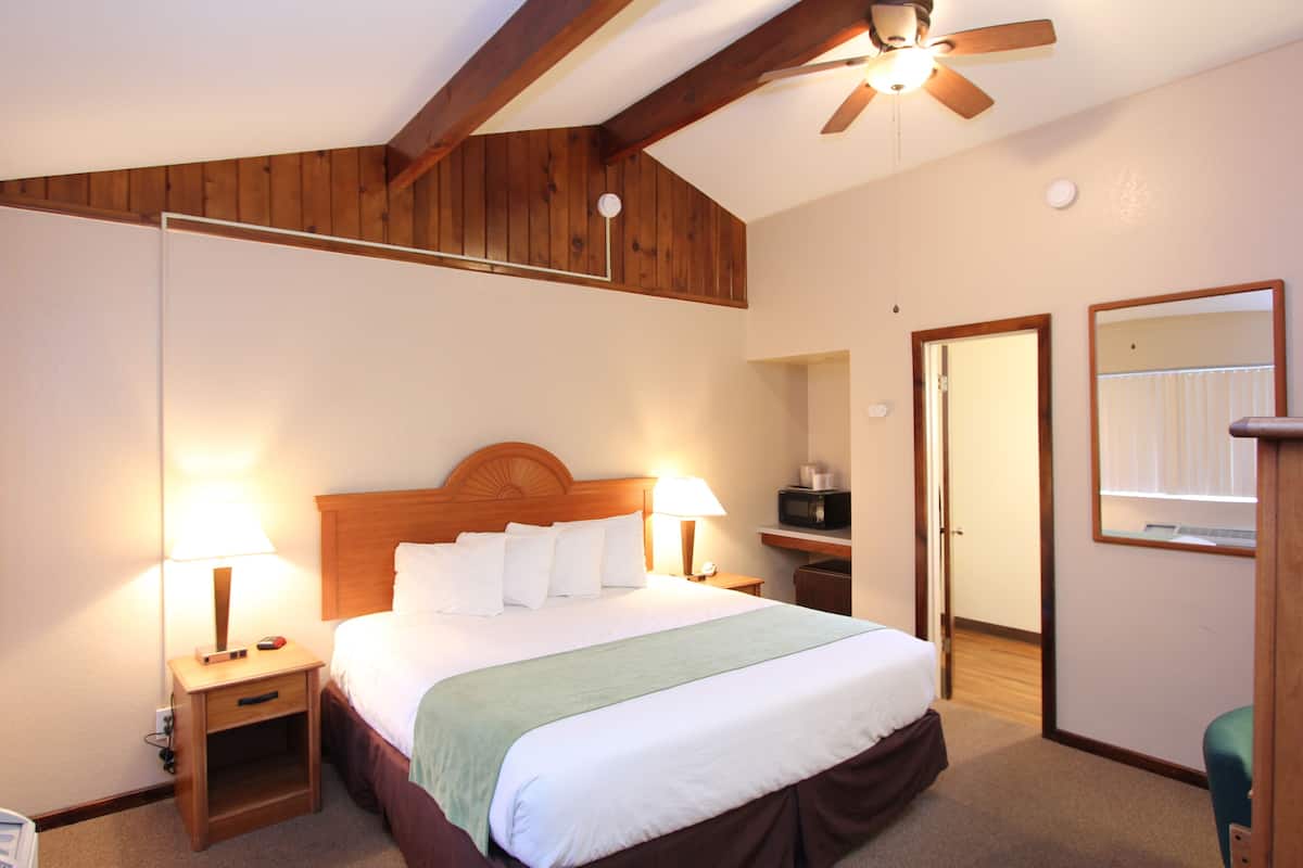 A hotel room with a wooden ceiling, a bed with white linens, two bedside tables with lamps, a green throw blanket, and a ceiling fan.