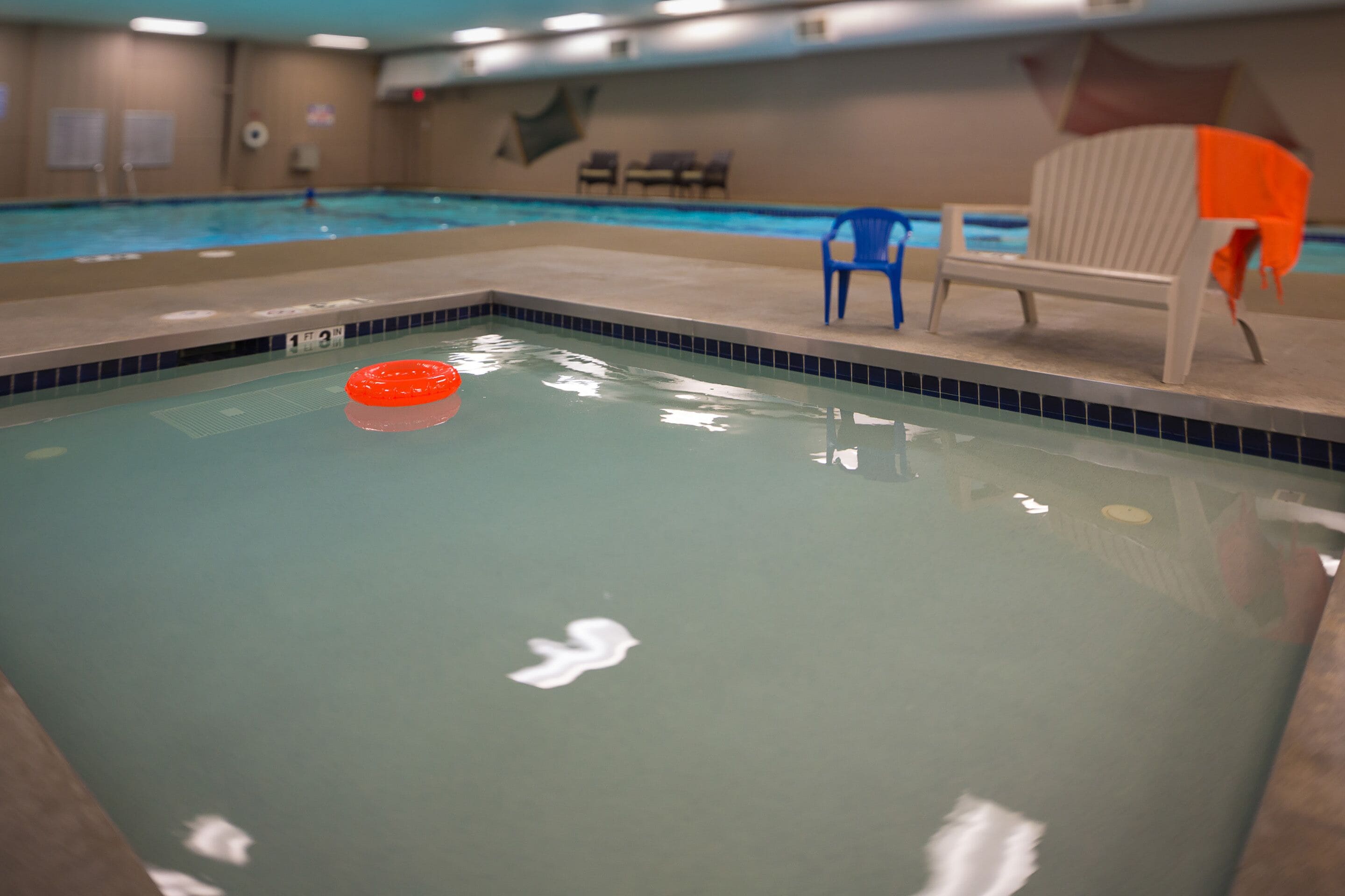 Piscina interna com uma cadeira azul e uma cadeira laranja perto da borda.