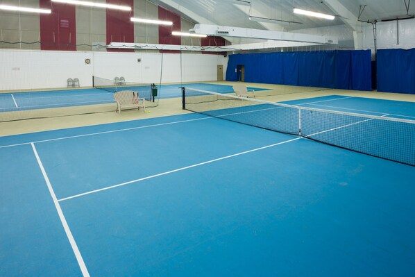 An indoor tennis court with a net, chairs, and a blue floor.