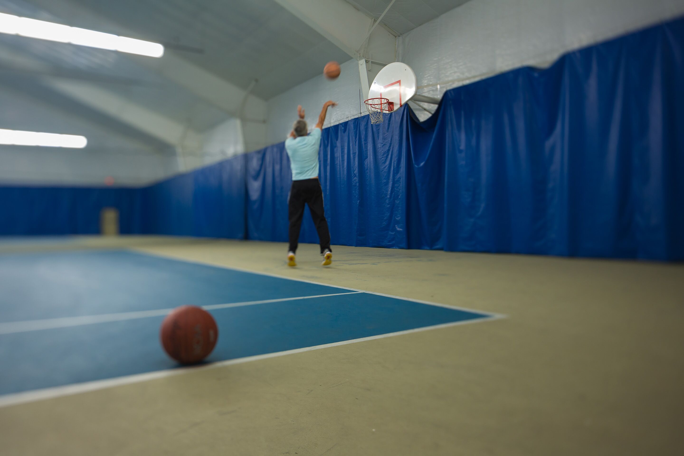 En basketplan inomhus med ett blått golv, en basketkorg och en person som spelar.