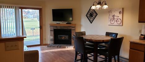A dining area with a fireplace, a television above it, and a dining table with chairs.