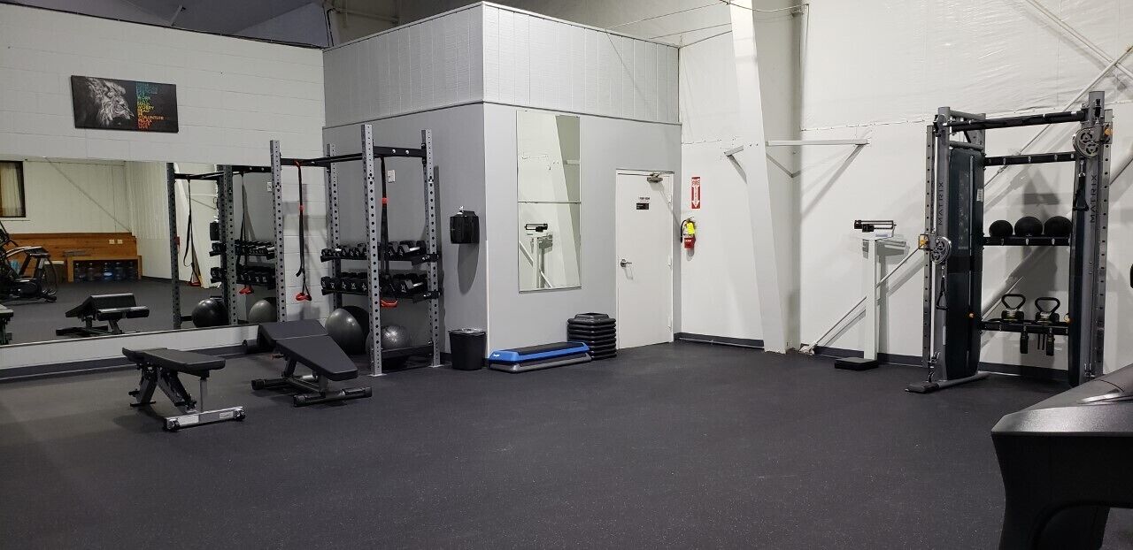 Un gimnasio con equipo de levantamiento de pesas, bancos y un espejo grande.