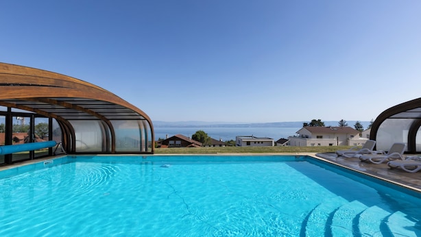 A swimming pool with a clear view of the ocean, surrounded by modern architecture and a few houses in the background. - Odalys Résidence Les Chalets d'Evian (Evian-les-Bains)