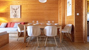 A wooden interior with a dining table set for four, a sofa with cushions, and a framed deer artwork on the wall. - Odalys Résidence Les Chalets d'Evian (Evian-les-Bains)