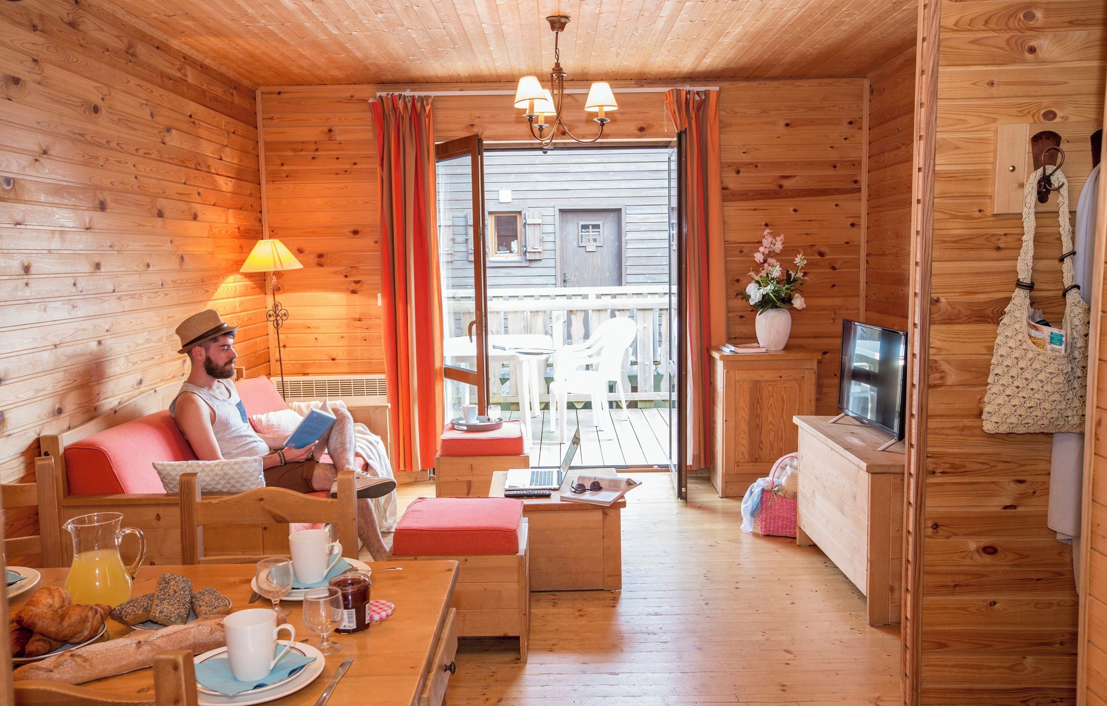 Viehättävä mökki, jossa on puuseinät, ruokailutila aamiaisineen, televisio ja parveke, jolta on kaunis näköala.