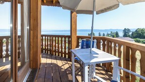 A wooden deck with a table and umbrella, overlooking a body of water. - Odalys Résidence Les Chalets d'Evian (Evian-les-Bains)