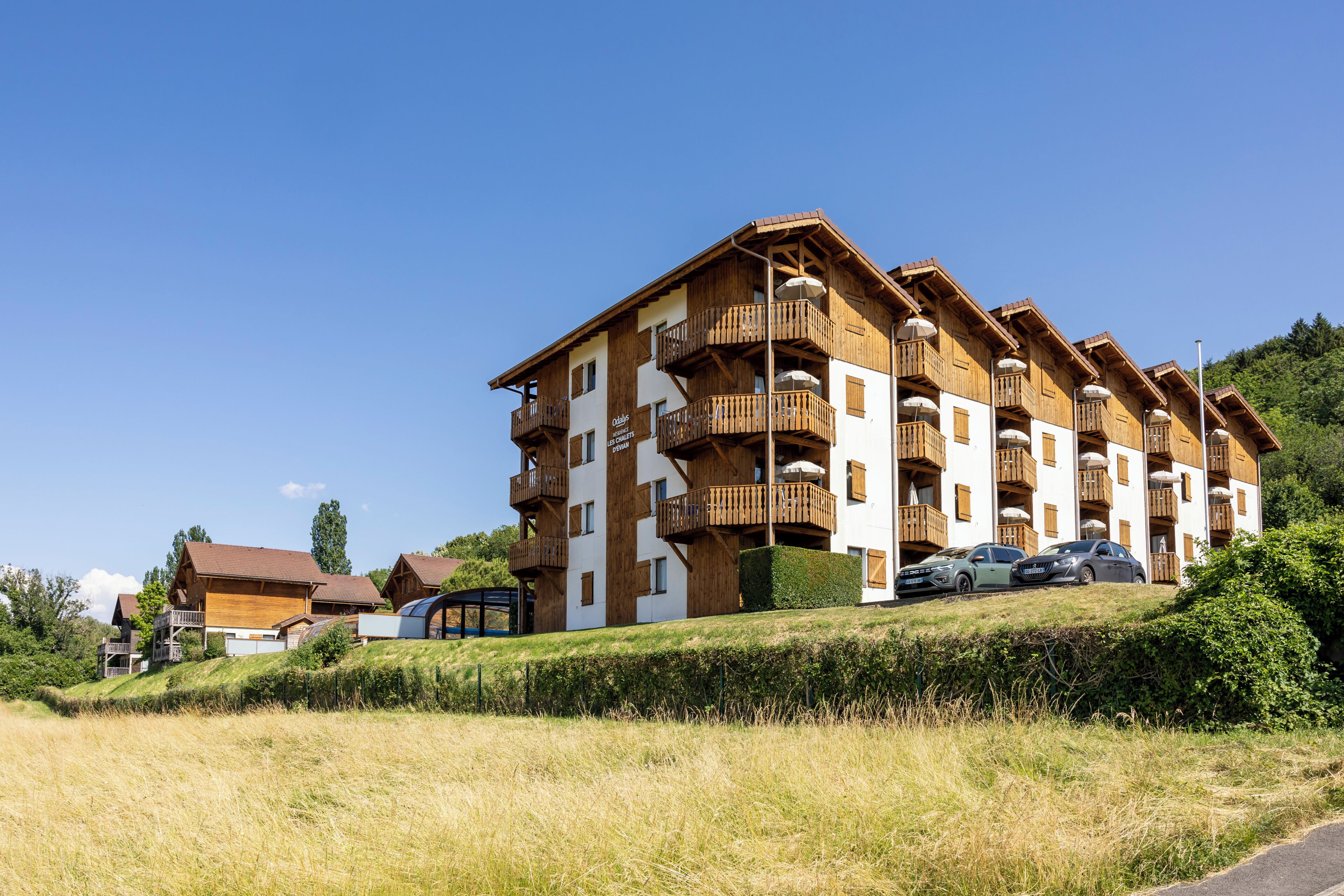 Un immeuble à plusieurs étages doté de balcons, d’un espace de stationnement et d’un parterre gazonné à l’avant.