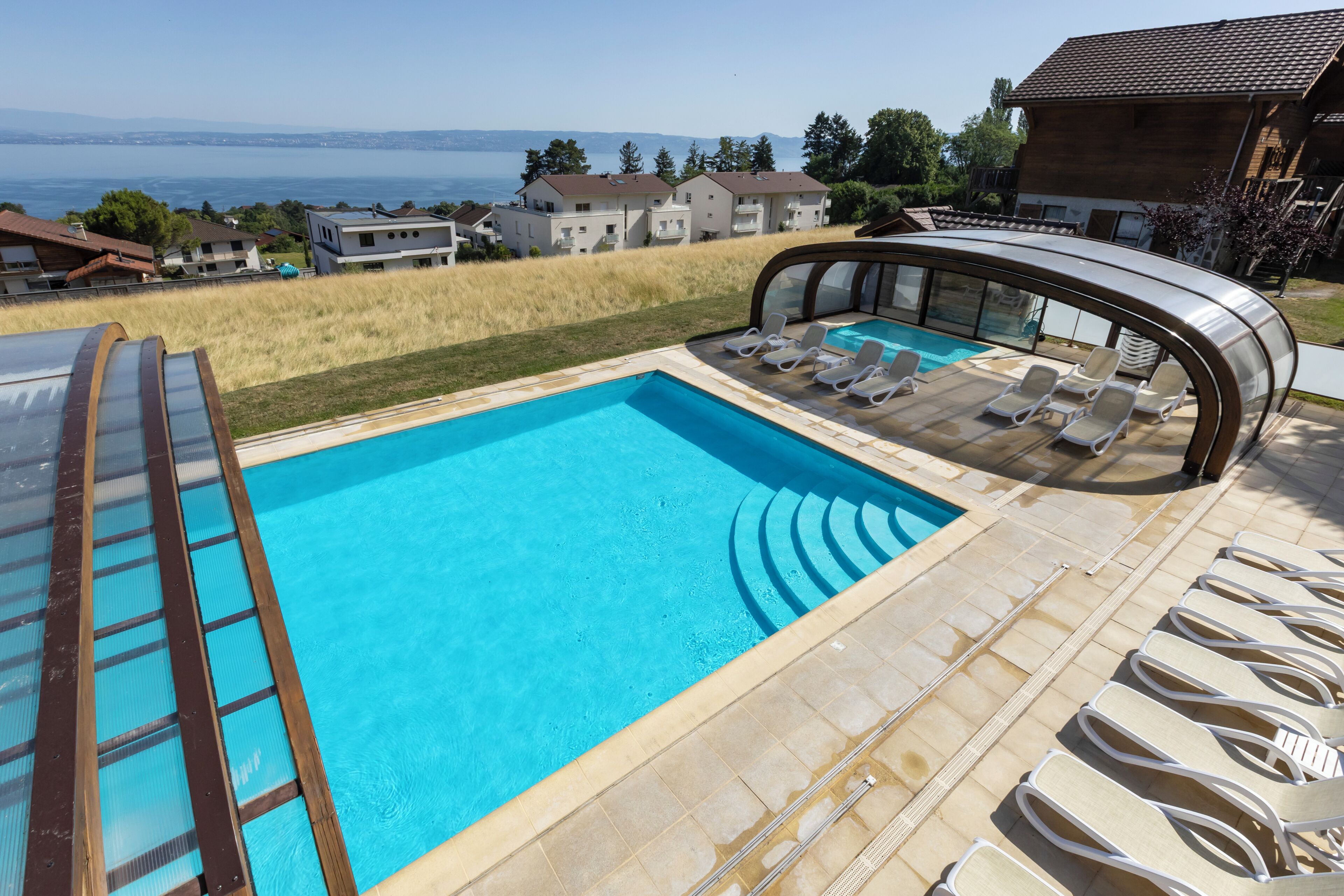 En swimmingpool med et glashegn, liggestole og havudsigt.