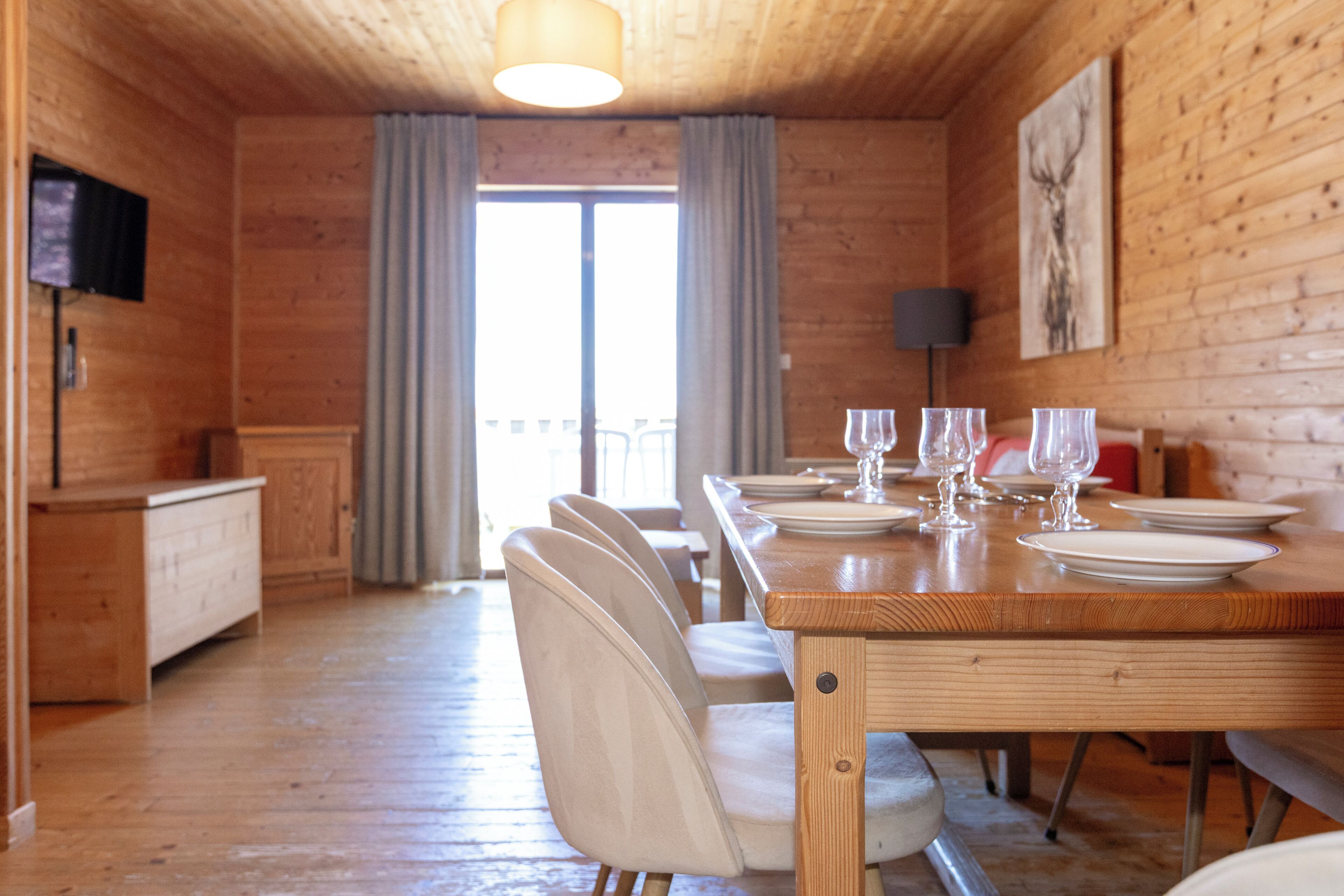 Een houten interieur met een eettafel voor zes personen, stoelen, een televisie en een schilderij aan de muur.