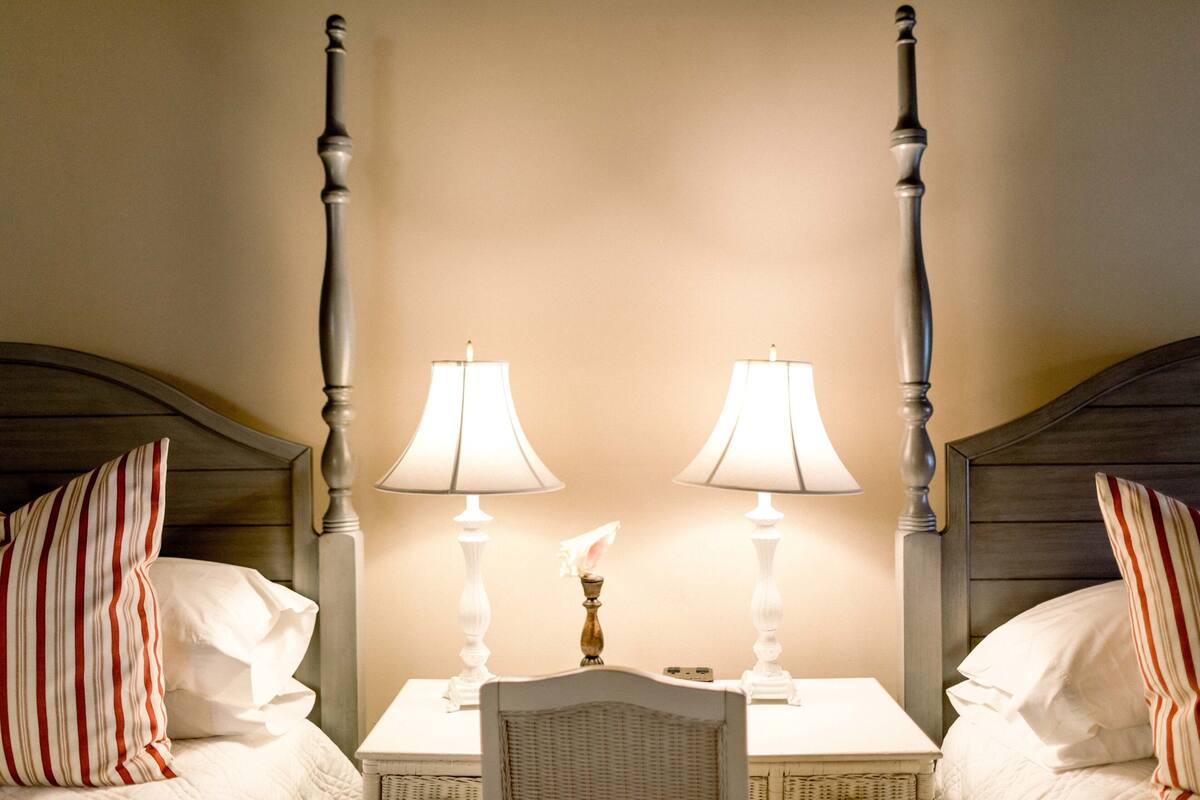 A hotel room with a four-poster bed, two bedside lamps, and a wicker chair.