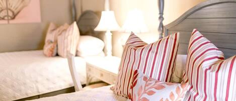 A bedroom with two beds, each with striped pillows and a bedside table with a lamp.