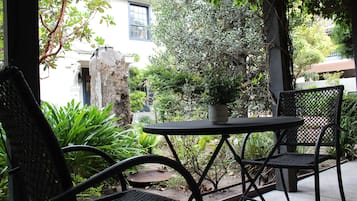 Une terrasse avec deux chaises en métal et une petite table ronde, entourée d’une végétation luxuriante et d’un mur de pierre.