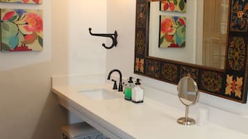 Un bagno con un lavandino bianco, uno specchio grande con cornice floreale, un porta asciugamani nero e un cestino.