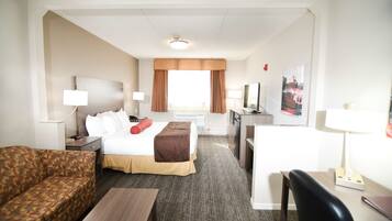 Quarto de hotel com cama, escrivaninha, cadeira, sofá e televisão.