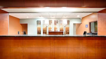 A hotel reception area with a marble counter, wooden paneling, and a large mirror.