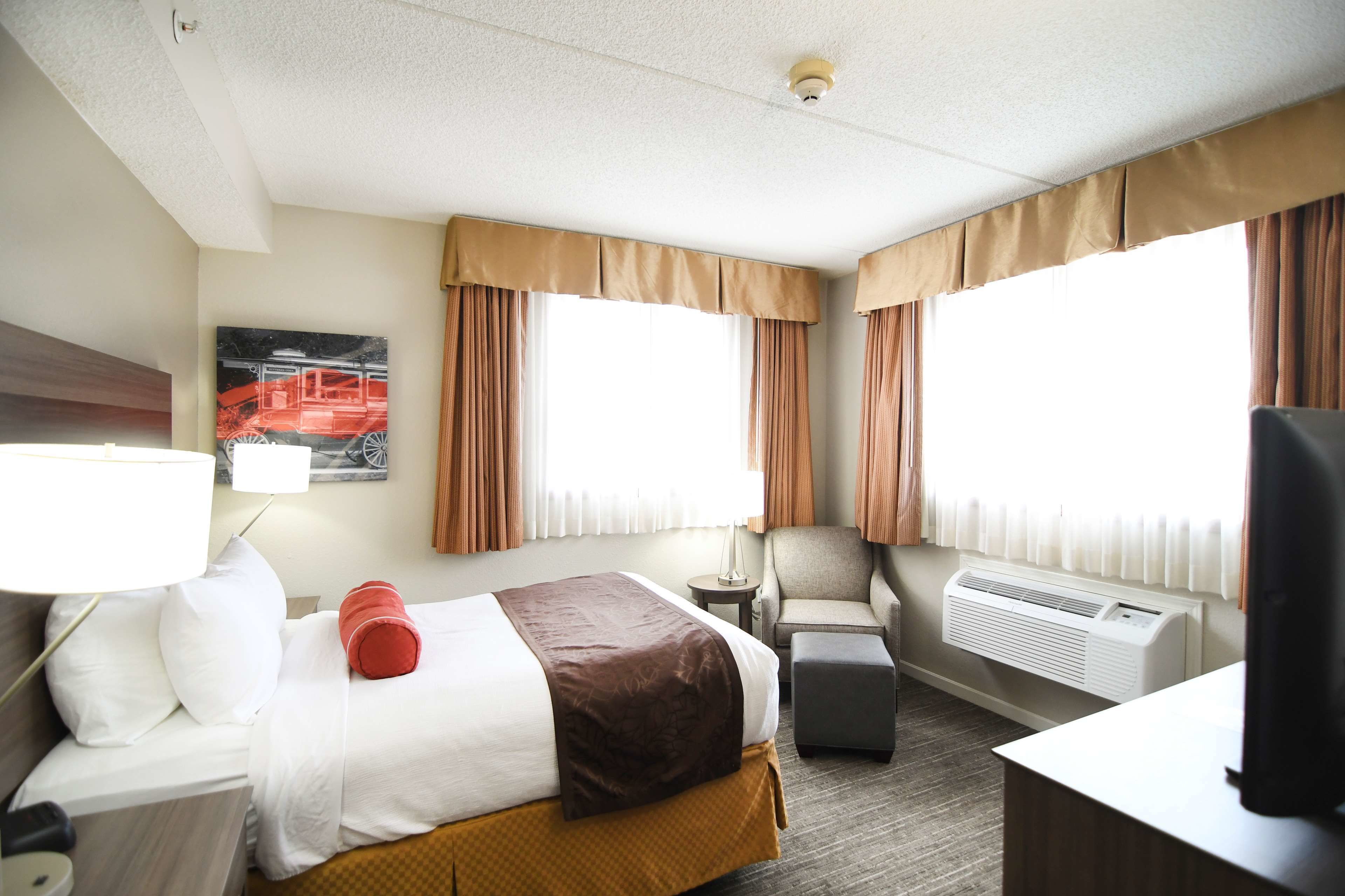 A hotel room with a bed, a chair, a desk, a lamp, and a television.