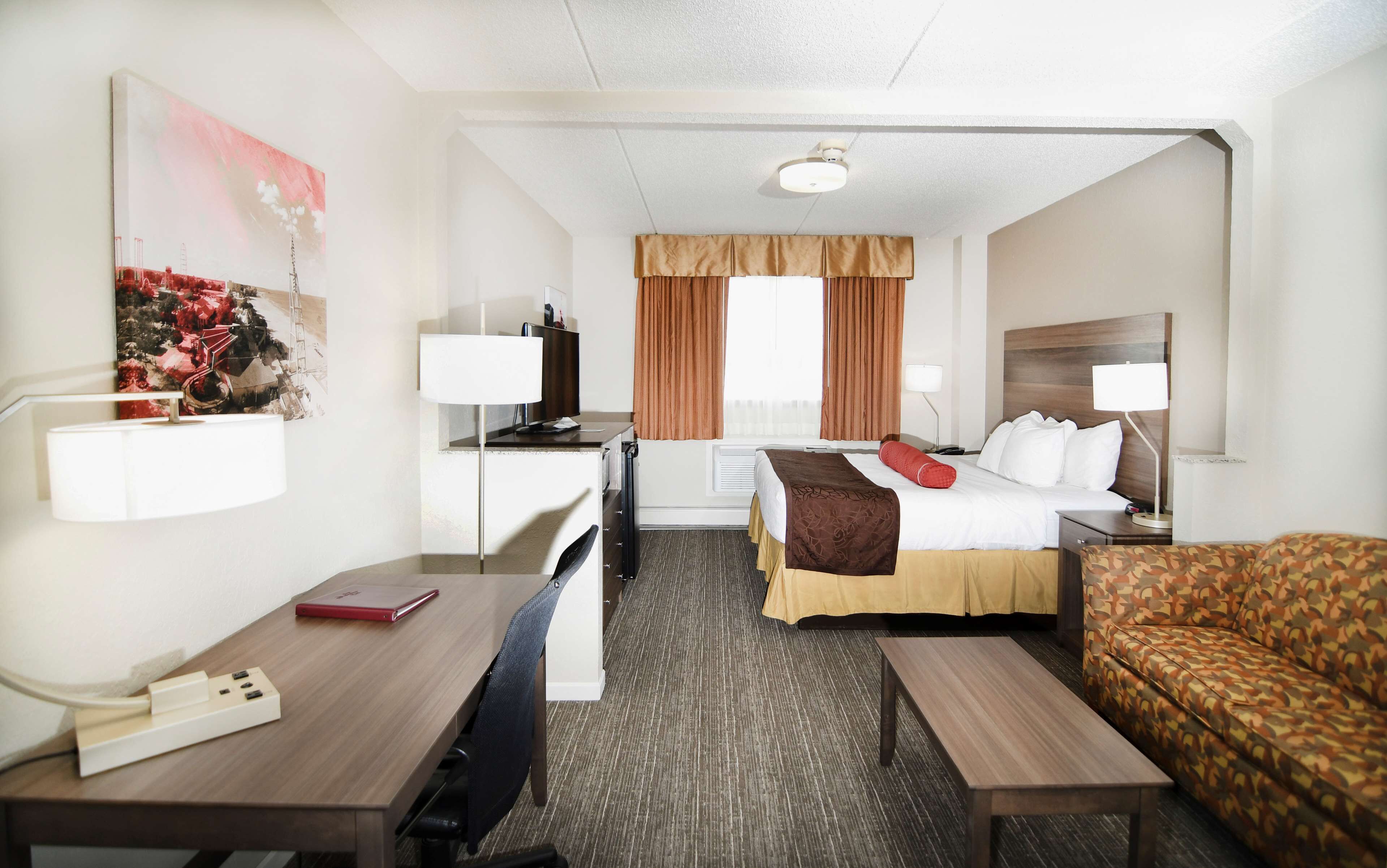 A hotel room with a bed, a desk, a chair, a sofa, and a TV.