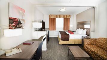 A hotel room with a bed, a desk, a chair, a sofa, and a TV.