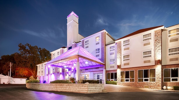 A hotel with a prominent tower, a covered entrance with purple lighting, and a well-lit facade. - Best Western Plus Sandusky Hotel & Suites (Sandusky)