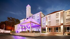 A hotel with a prominent tower, a covered entrance with purple lighting, and a well-lit facade. - Best Western Plus Sandusky Hotel & Suites (Sandusky)