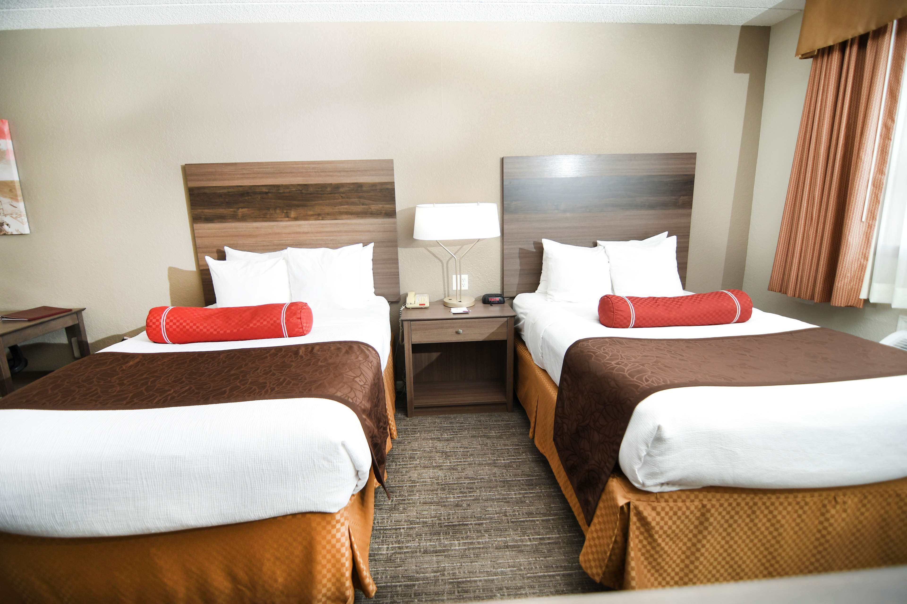 A hotel room with two beds, a nightstand, a lamp, and a window with curtains.