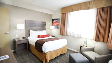 Une chambre d’hôtel avec un lit, une chaise, une table de chevet, une lampe et une fenêtre avec des rideaux.