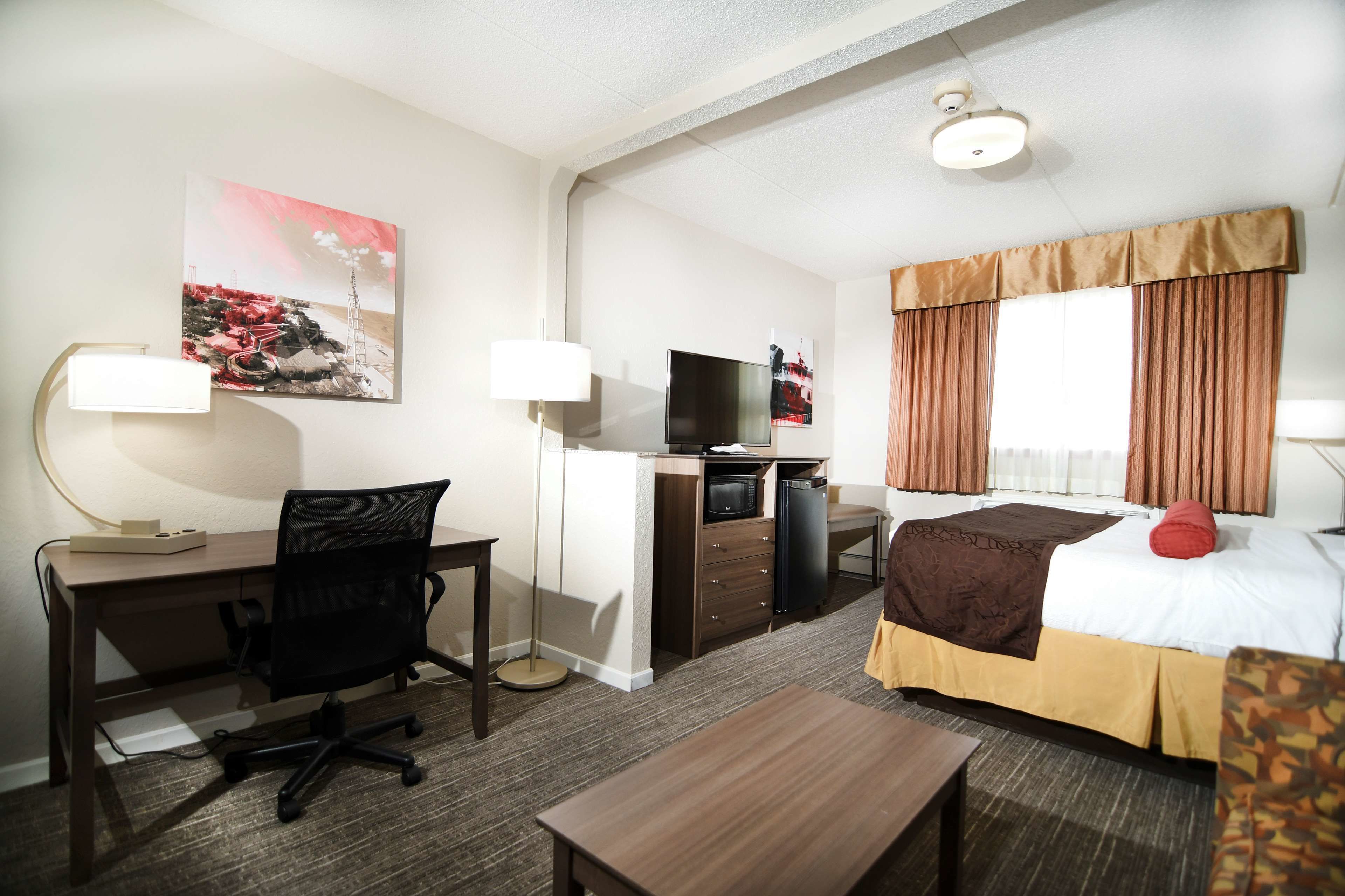 Una habitación de hotel con escritorio, silla, cama, televisor y un cuadro en la pared.