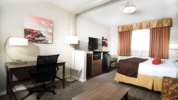 Una habitación de hotel con escritorio, silla, cama, televisor y un cuadro en la pared.