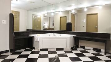 A bathroom with a checkered floor, a white bathtub, and a large mirror.