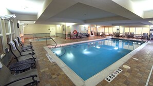 Una piscina interior con suelo de baldosas, sillas de descanso y zona de la piscina despejada.