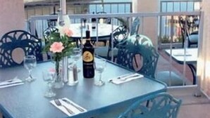 Une table dressée pour deux personnes, avec une bouteille de vin, des verres et un vase rempli de fleurs.