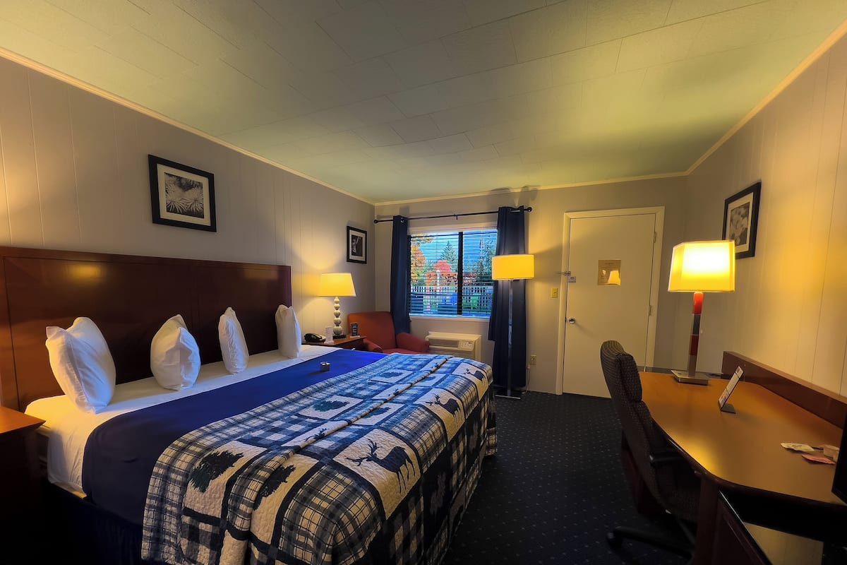 Ein Hotelzimmer mit einem großen Bett, zwei Nachttischen mit Lampen, einem Schreibtisch mit Stuhl, einem Fenster mit Vorhängen und einer Tür.