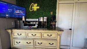 A bar area with a neon sign, coffee machines, and a TV displaying weather information. - American Boutique Inn - Lakeview (Mackinaw City)