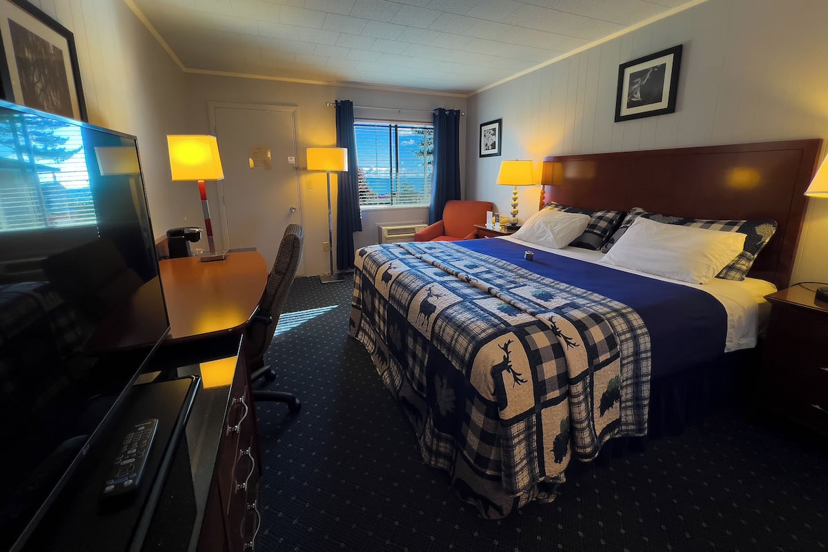 Ein Hotelzimmer mit Bett, Schreibtisch, Stuhl, Fernseher und einem fensterbepflanzten Fenster.
