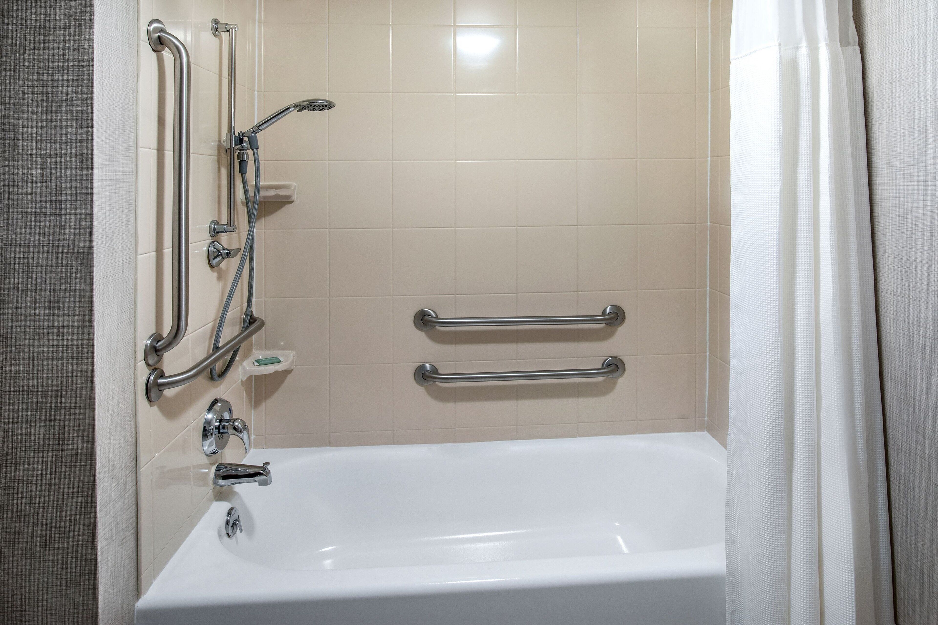 Ein Badezimmer mit einer weißen Badewanne, Haltegriffen und einer Duschbrause.