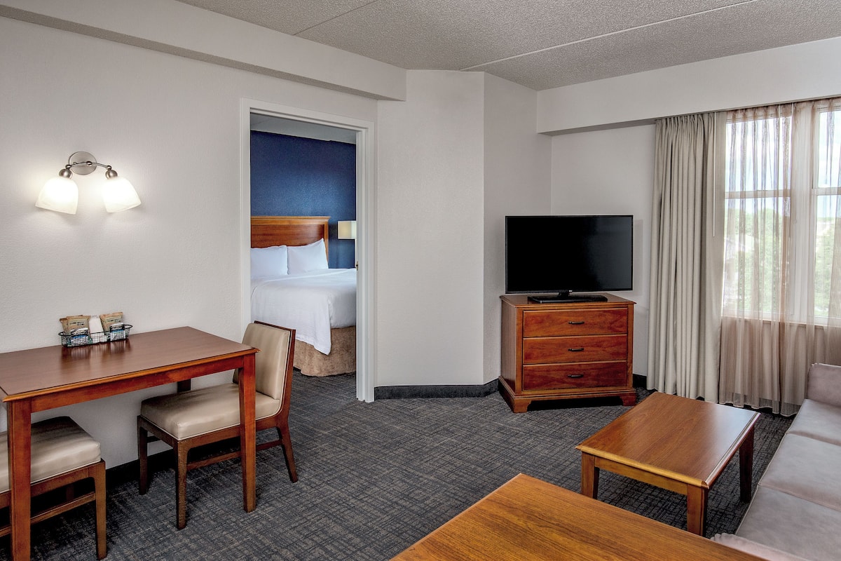 A hotel room with a bed, a desk, a television, a dresser, and a sofa.