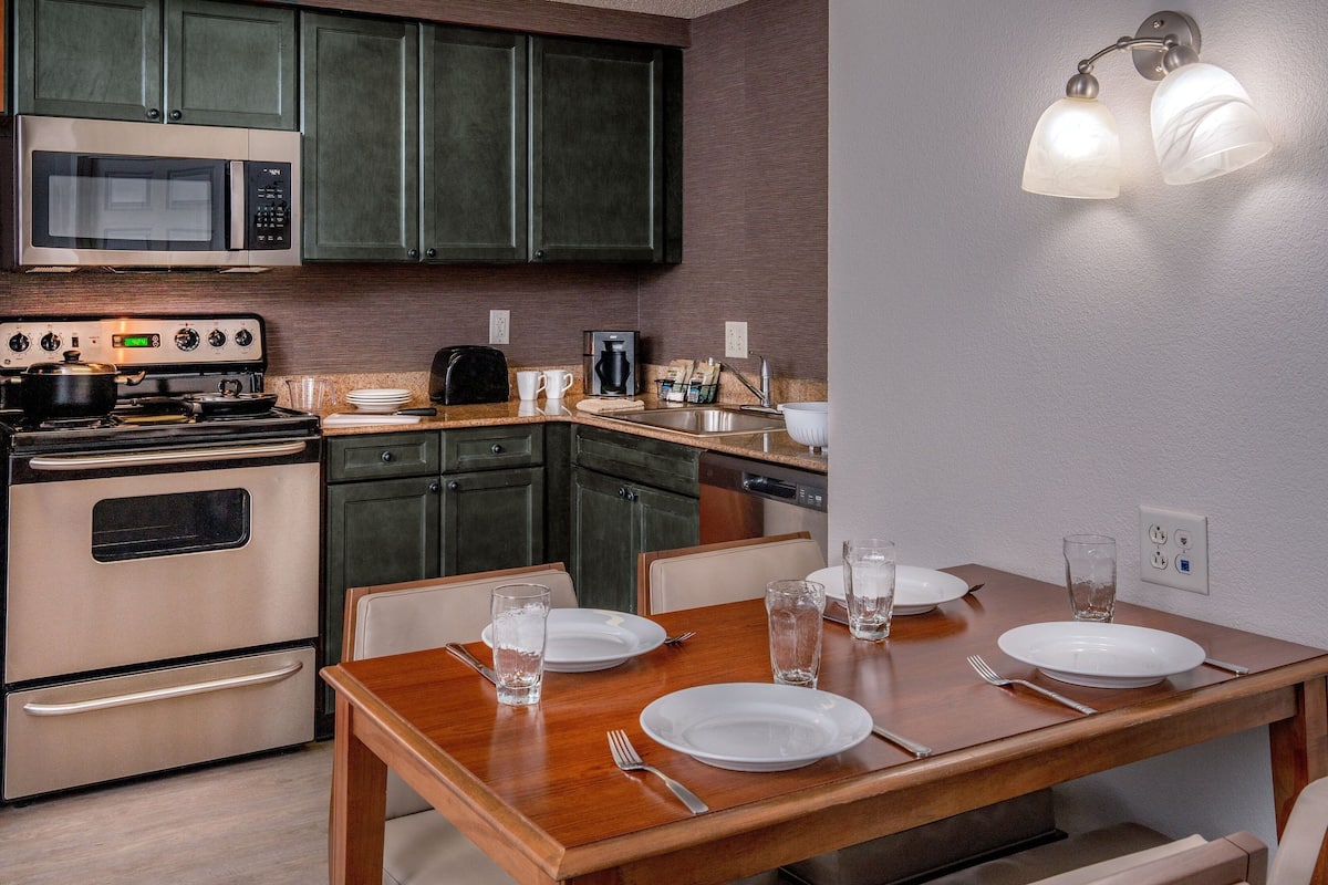 A kitchen with a microwave, stove, and dishwasher. There is a dining table with plates and glasses.