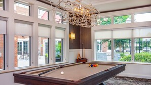 A pool table with a billiard cue and balls, large windows, and a patterned carpet.