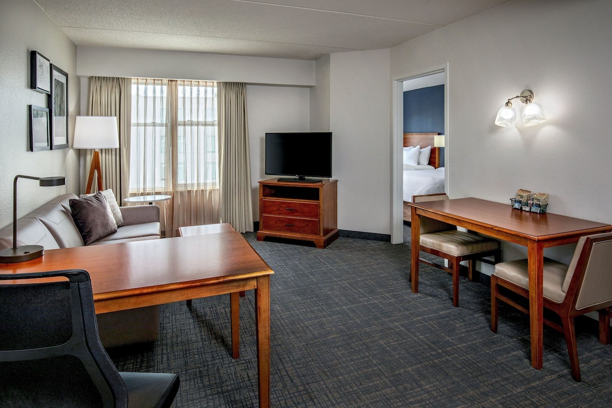 A hotel room with a sofa, a wooden table, a TV, a desk, and a chair.