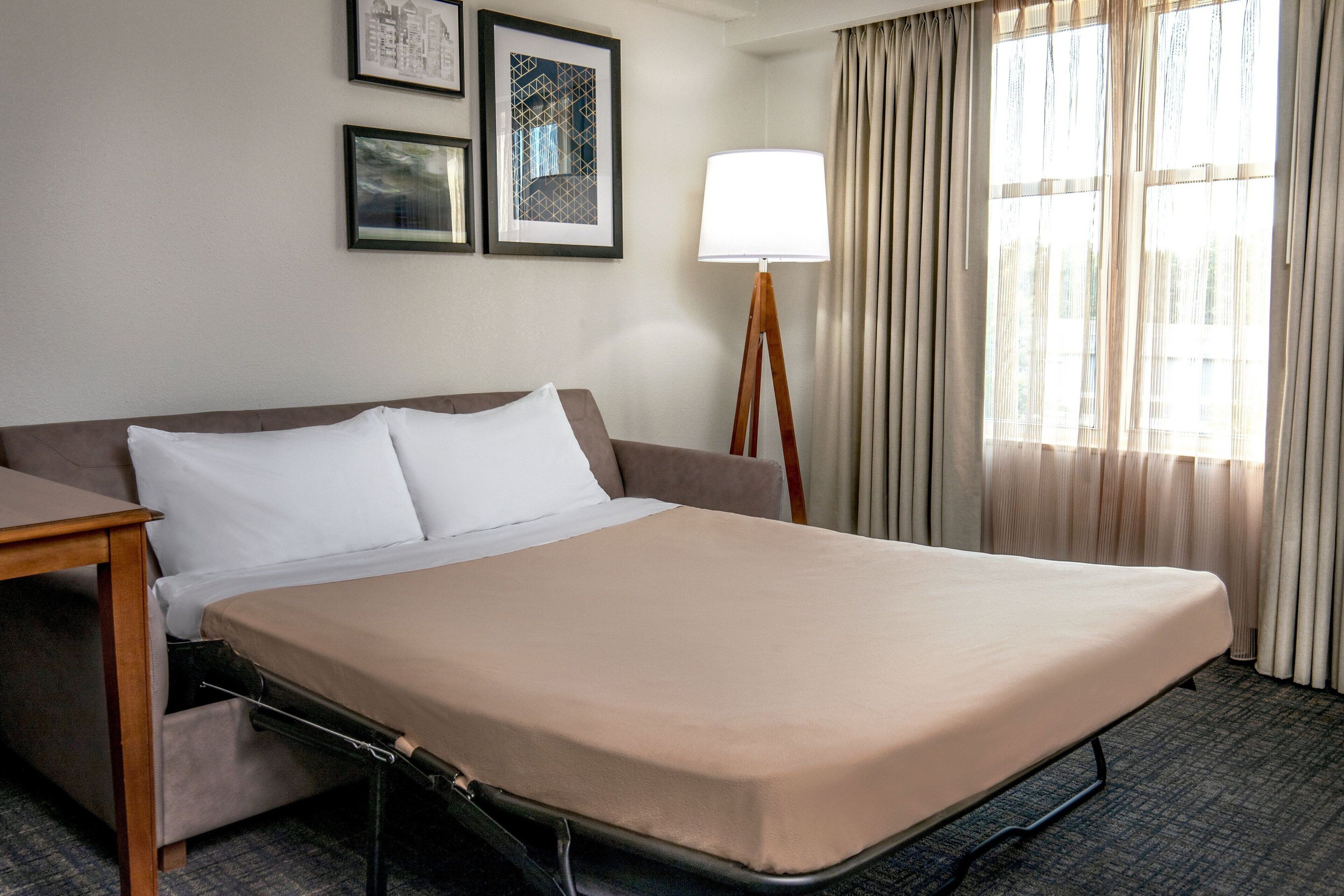 A hotel room with a bed, a bedside table, a lamp, and a window with curtains.