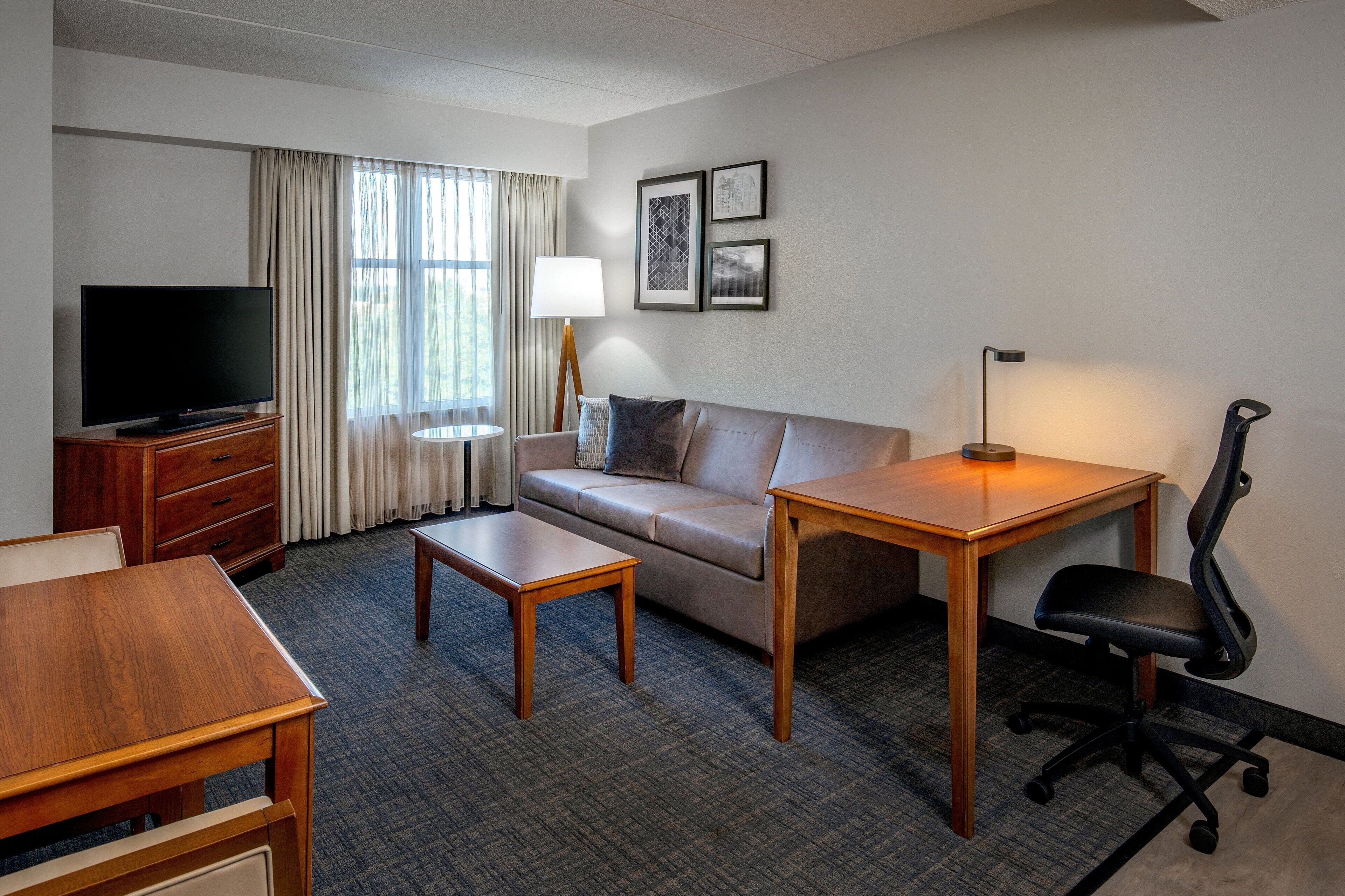 A hotel room with a TV, sofa, two tables, a desk, and a chair.