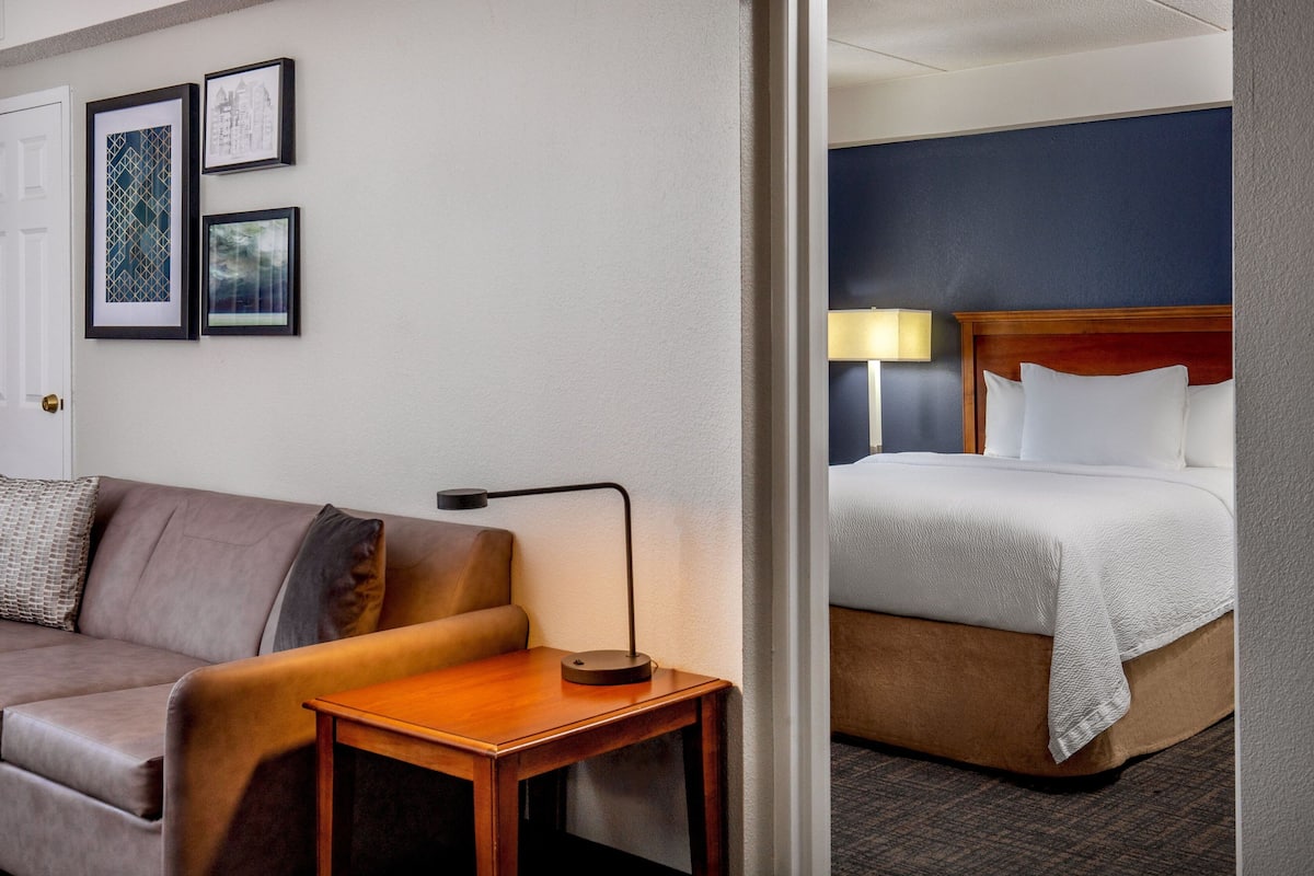 A hotel room with a sofa, a bedside table with a lamp, and a bed with a headboard.
