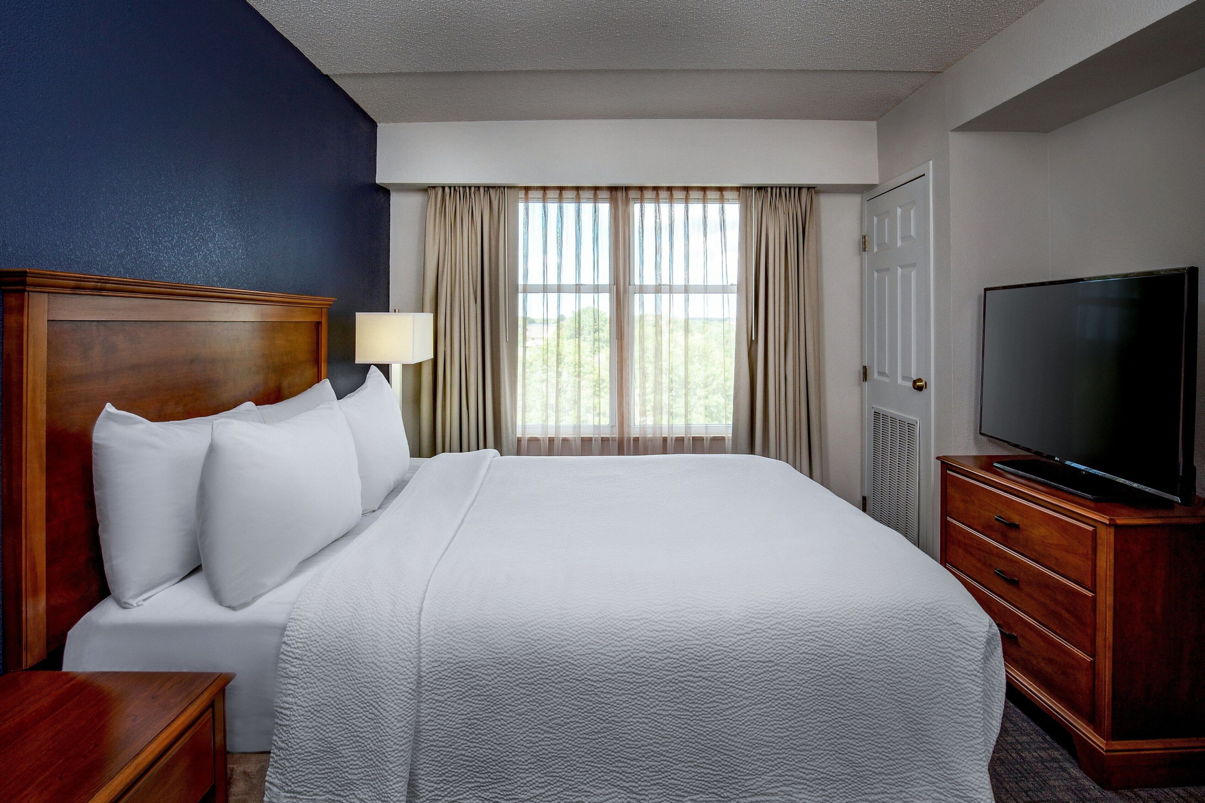 A hotel room with a large bed, a TV, a nightstand, and a window with curtains.