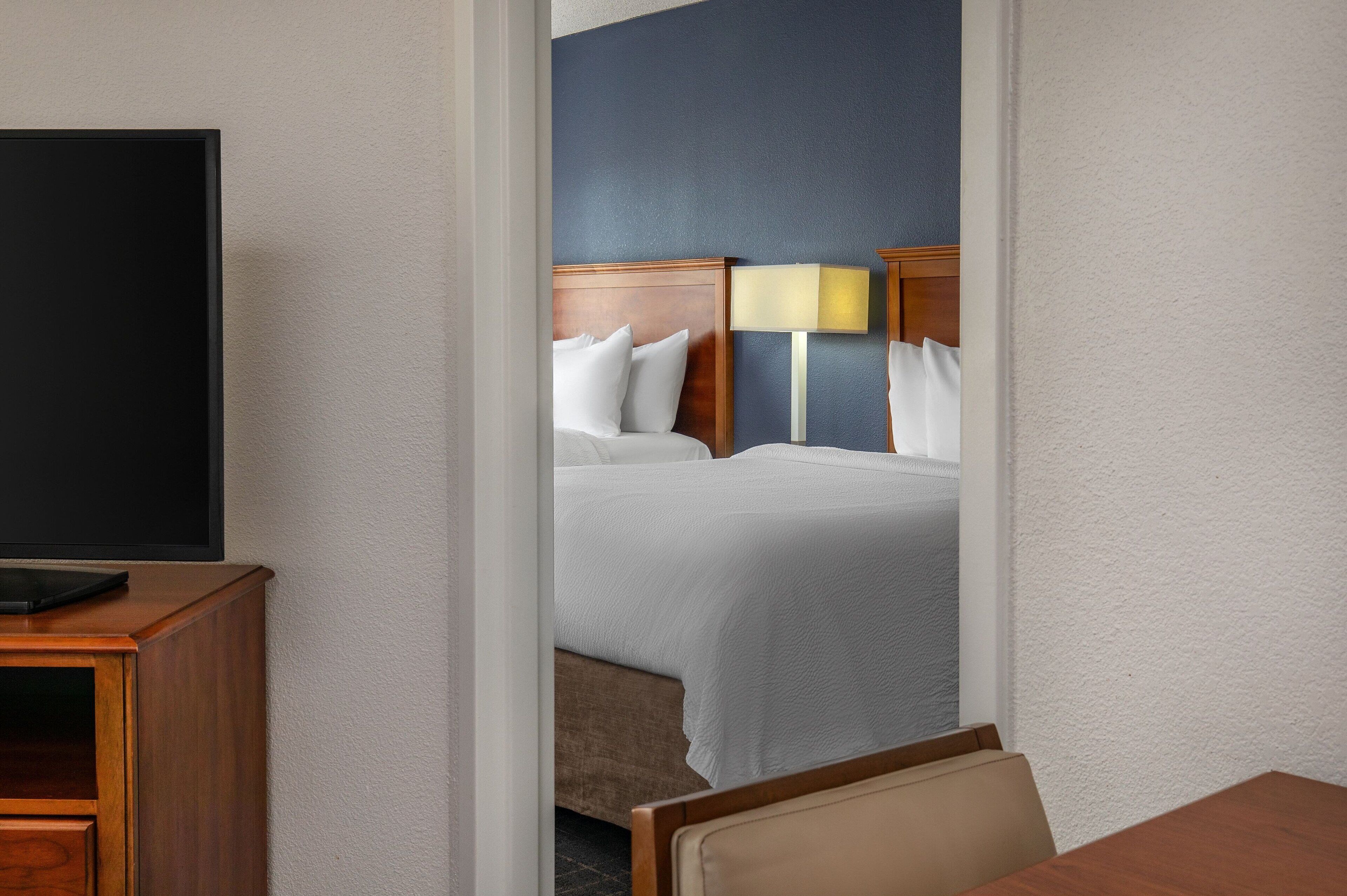 A hotel room with a bed, a bedside table, a lamp, and a television.