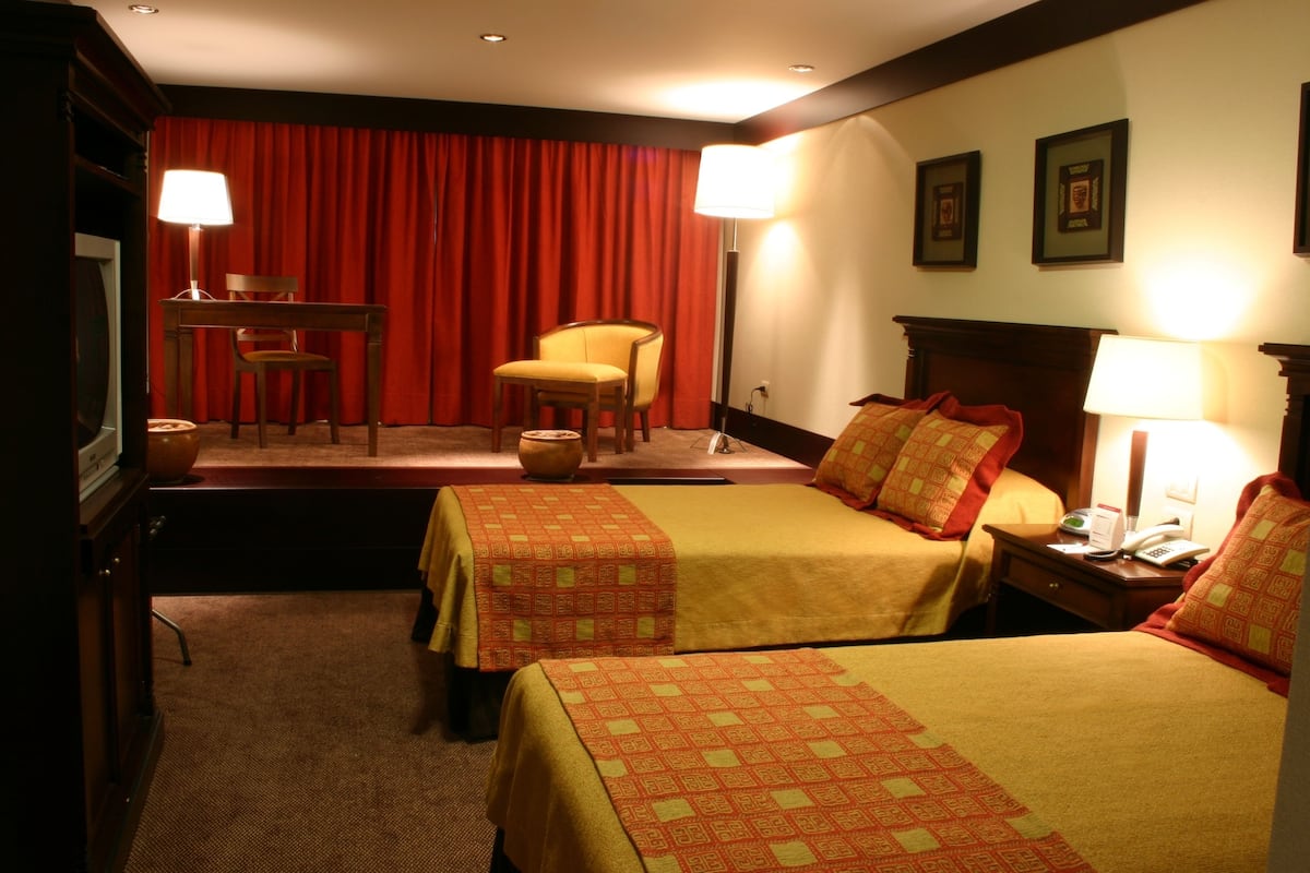 Ein Hotelzimmer mit zwei Betten, einem Schreibtisch, einem Sessel und einem Fernseher.