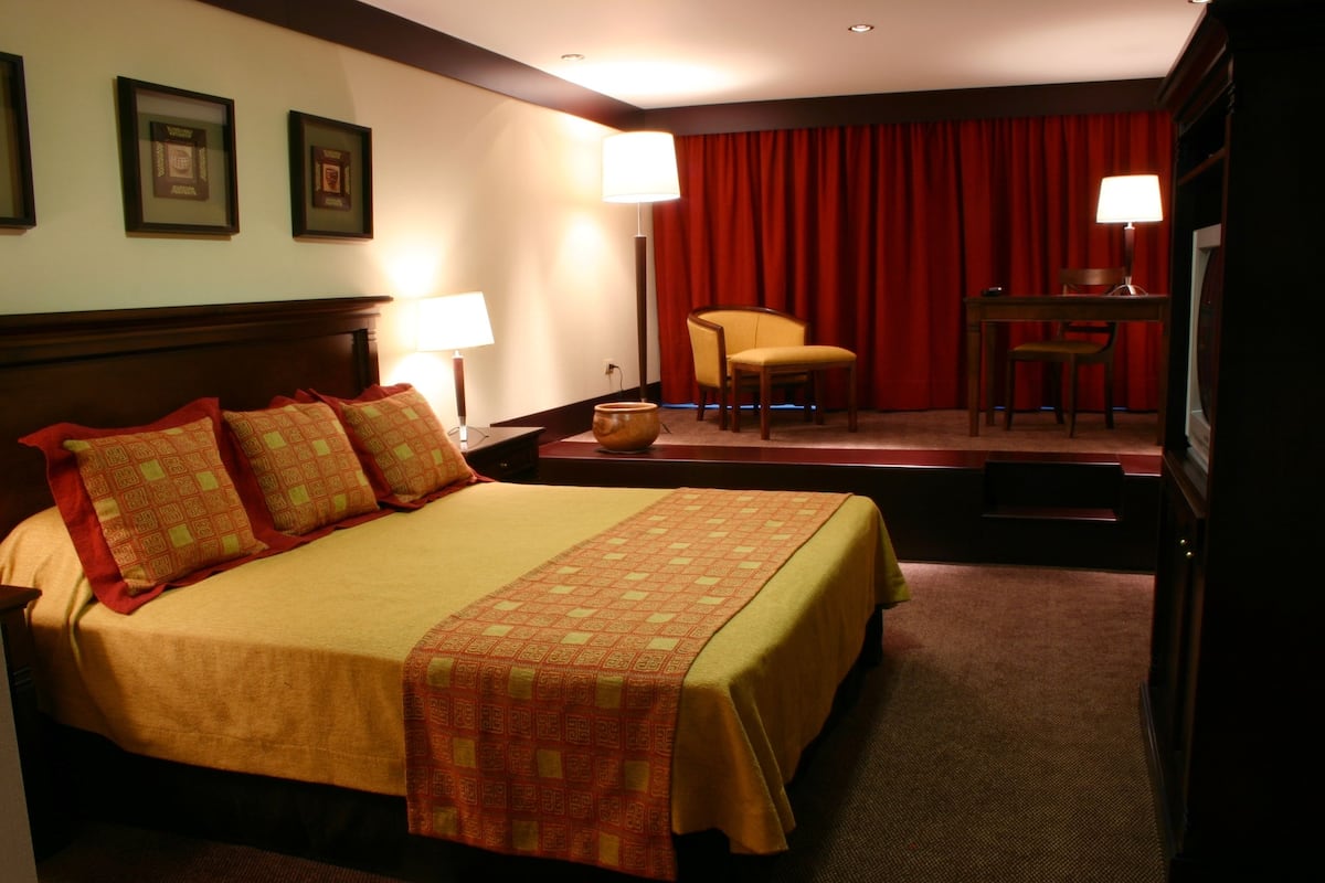 Ein Hotelzimmer mit einem großen Bett, einem Sessel, einem Schreibtisch und einem Fernseher.