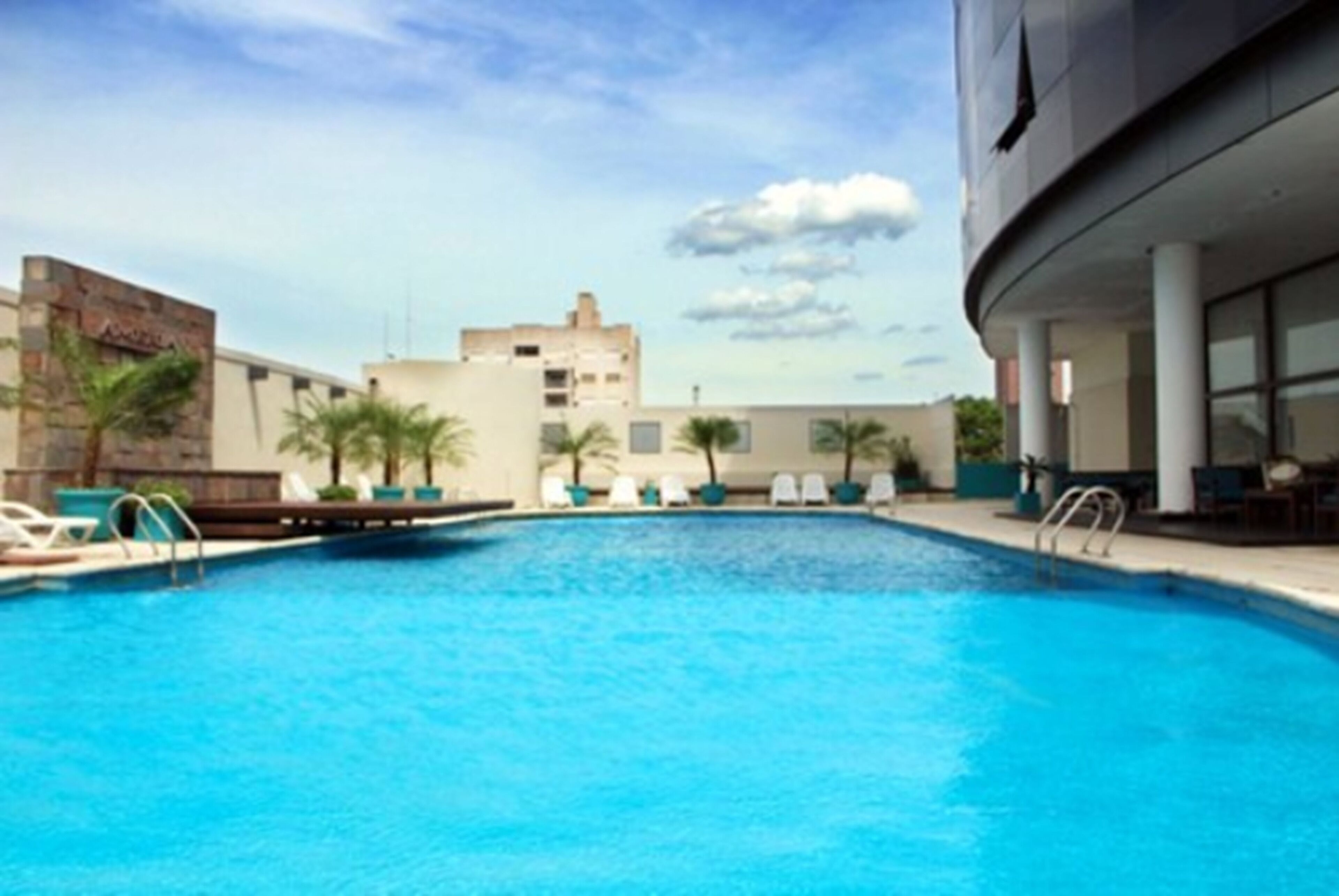 Una piscina con sillones de descanso y palmeras, rodeada de edificios.