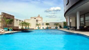 Una piscina con sillones de descanso y palmeras, rodeada de edificios.